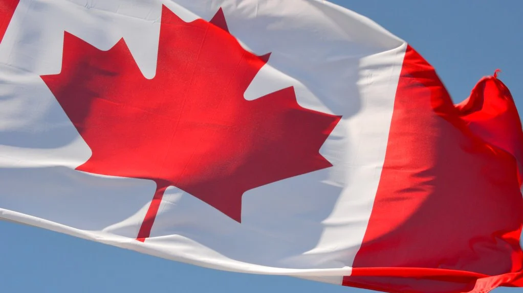 Canadian flag with a silhouette of a person looking towards a cityscape.