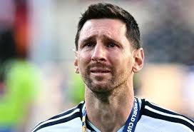 Lionel Messi looking somber, holding a football.